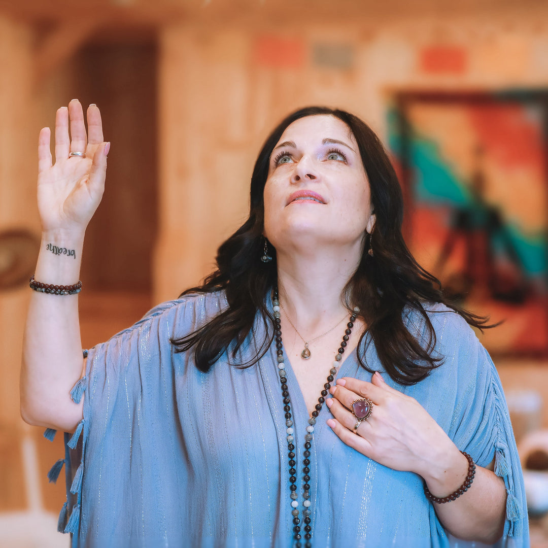 Woman in a blue top with raised hand in a room with colorful abstract art on the wall.