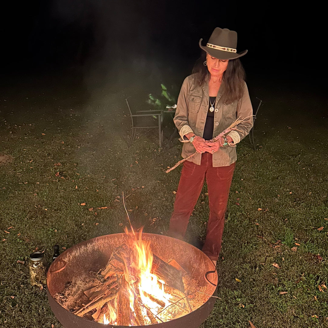 Person standing by a fire pit at night wearing a cowboy hat.