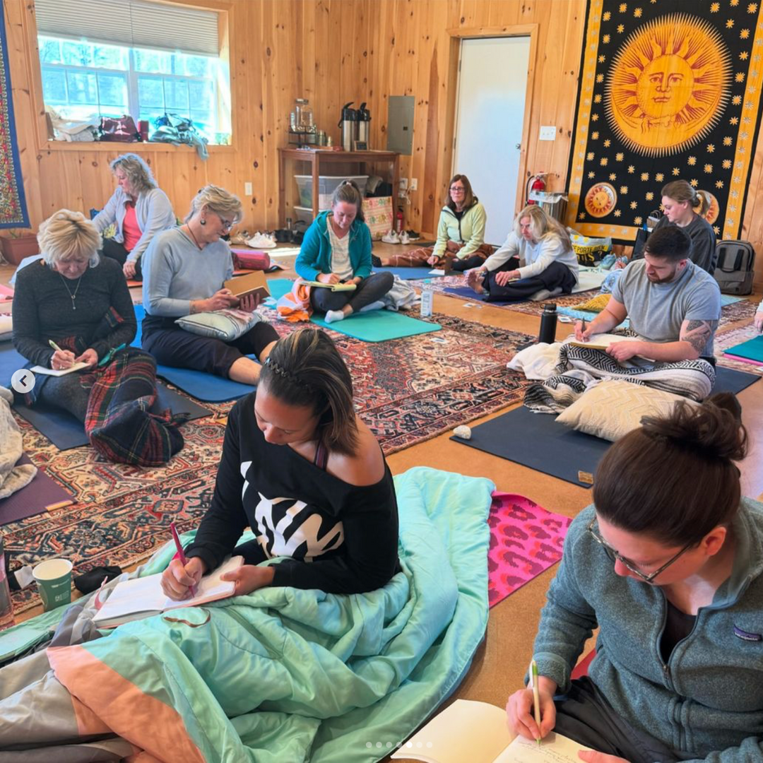 Group of people sitting on the floor in a room with wooden walls, participating in a workshop or class.