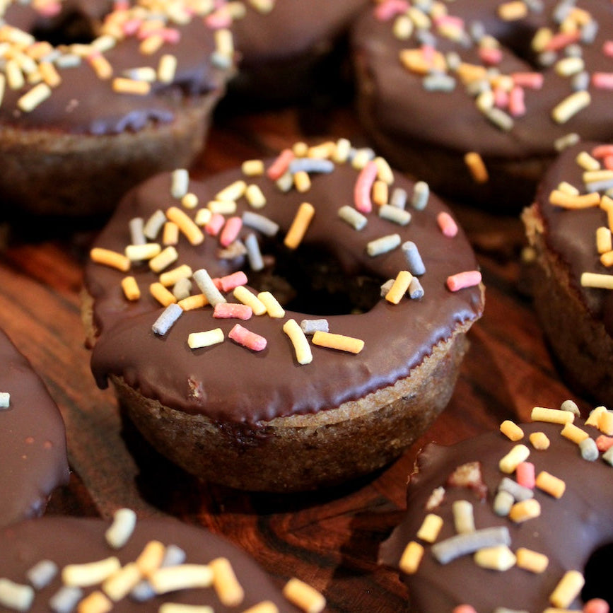 Chocolate-covered donuts with pastel sprinkles sitting on a wooden surface.