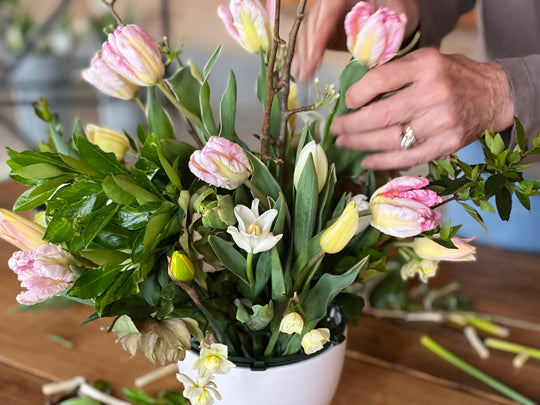 Person arranging flowers in a pot with tulips and other plants.
