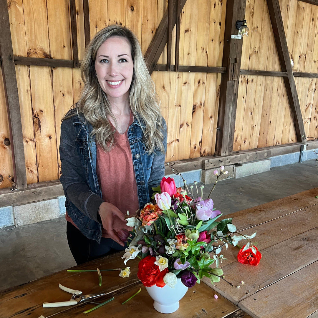 Woman arranging flowers at a wooden table in a rustic setting