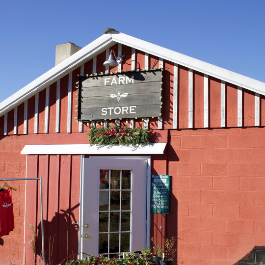 Red cinderblock building with wooden sign that says "Farm Store" above the door. Evergreens and red berries arrangement under the sign.