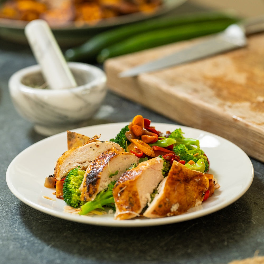 Plated dish of chicken and vegetables on a kitchen counter with a mortar and pestle in the background.