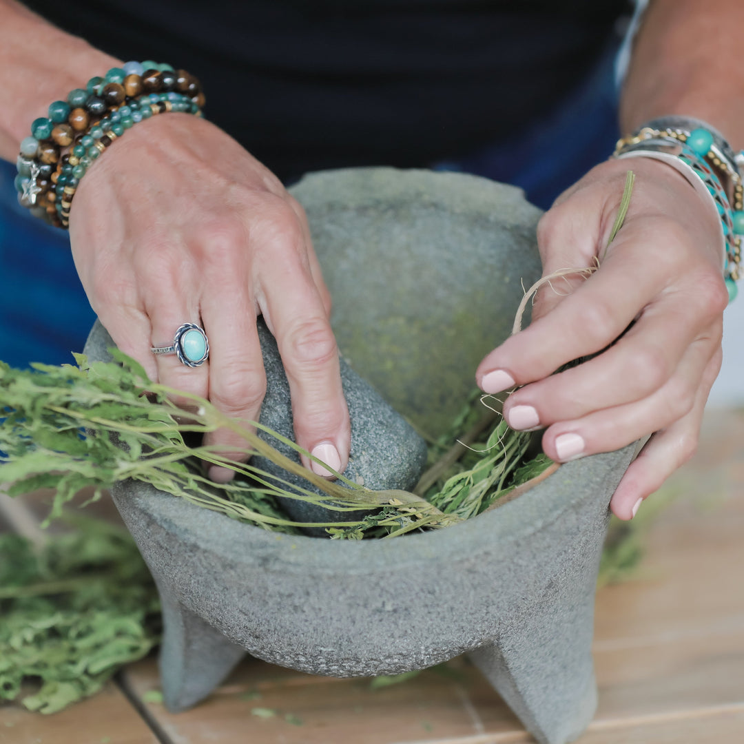 Person using a mortar and pestle with herbs on a wooden surface