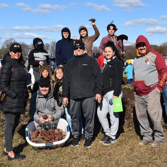 Group of people outdoors in a field with a person holding a basket of potatoes.