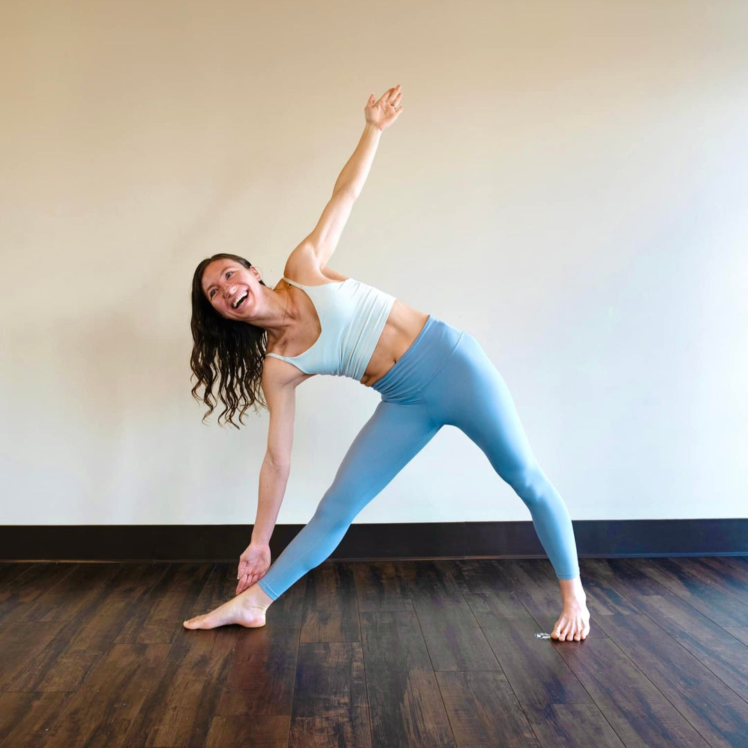 Woman in a yoga pose on a wooden floor with a white wall background