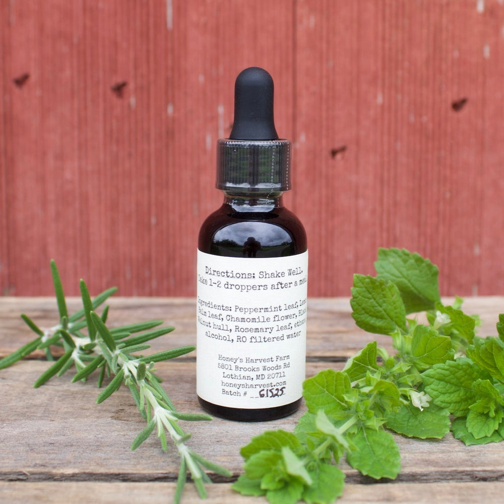 Bottle of tincture with a label on a wooden surface with green leaves and herbs, against a red wooden background.