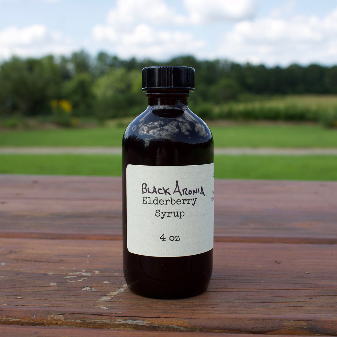 Bottle of Black Aronia Elderberry Syrup on a wooden surface with a natural background