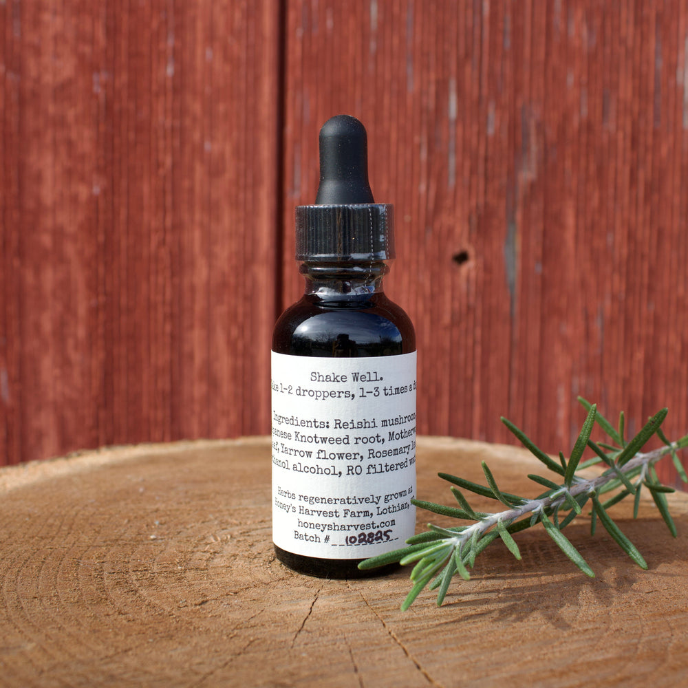 Bottle of tincture with a dropper on a wooden surface next to a sprig of rosemary, against a wooden background.