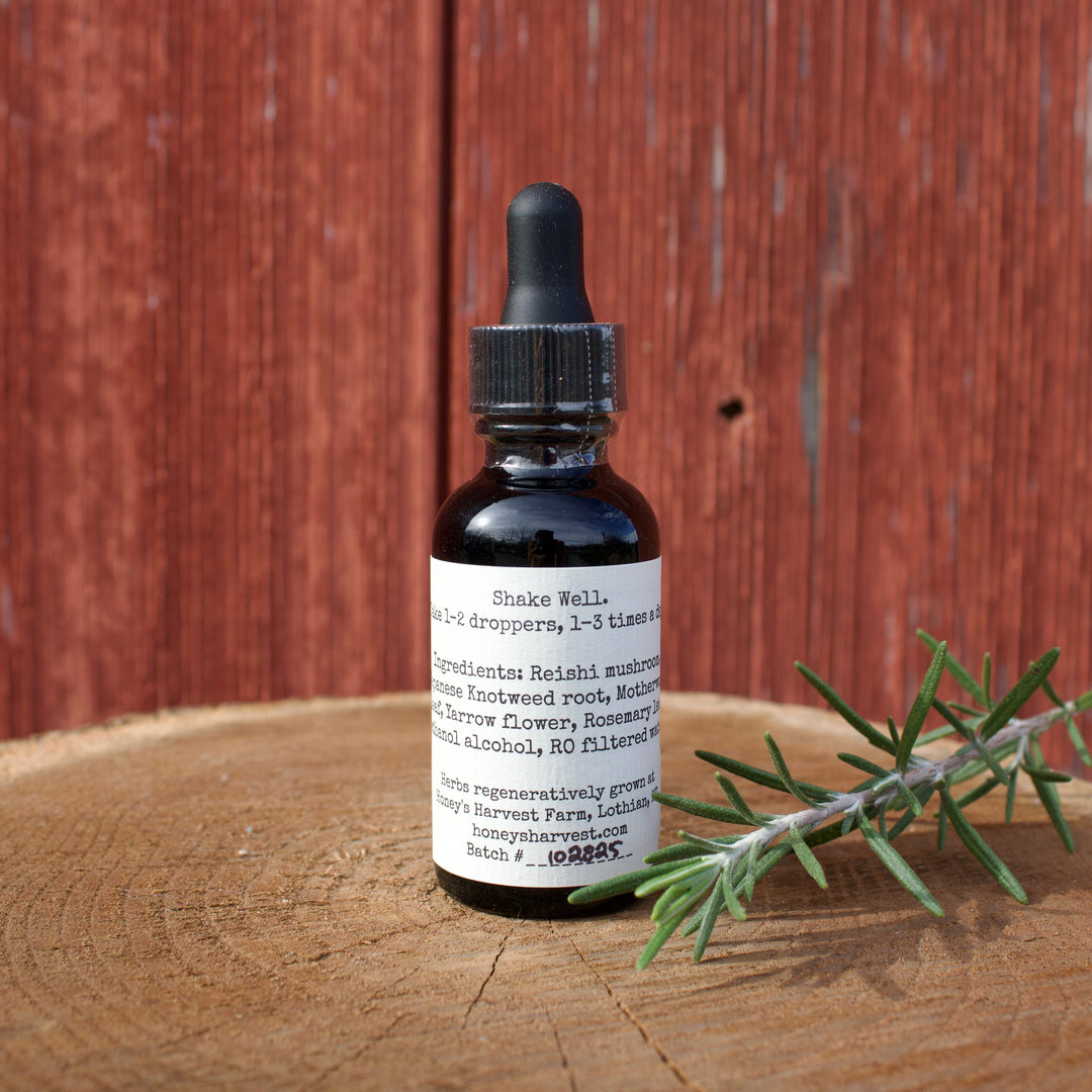 Bottle of tincture with a dropper on a wooden surface next to a sprig of rosemary, against a wooden background.