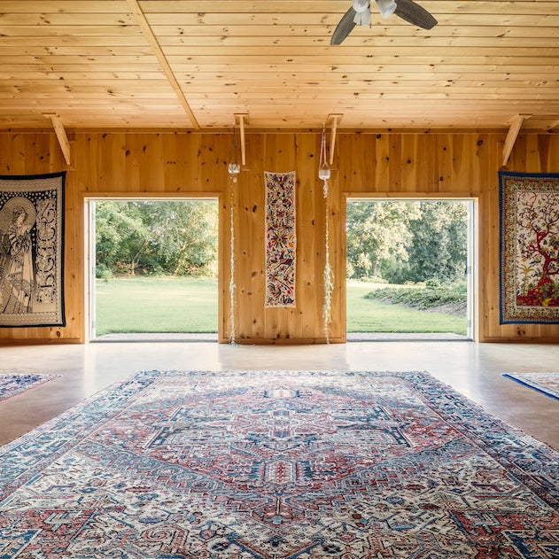 Large room with wooden walls and ceiling, featuring a large rug and decorative elements.