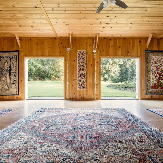 Large room with wooden walls and ceiling, featuring a large rug and decorative elements.