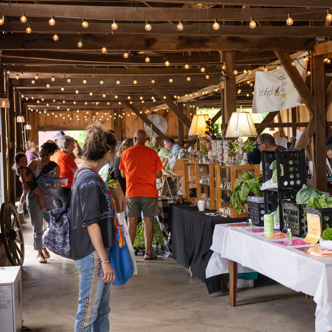 People shopping at an indoor farmers market with tables displaying produce and goods.