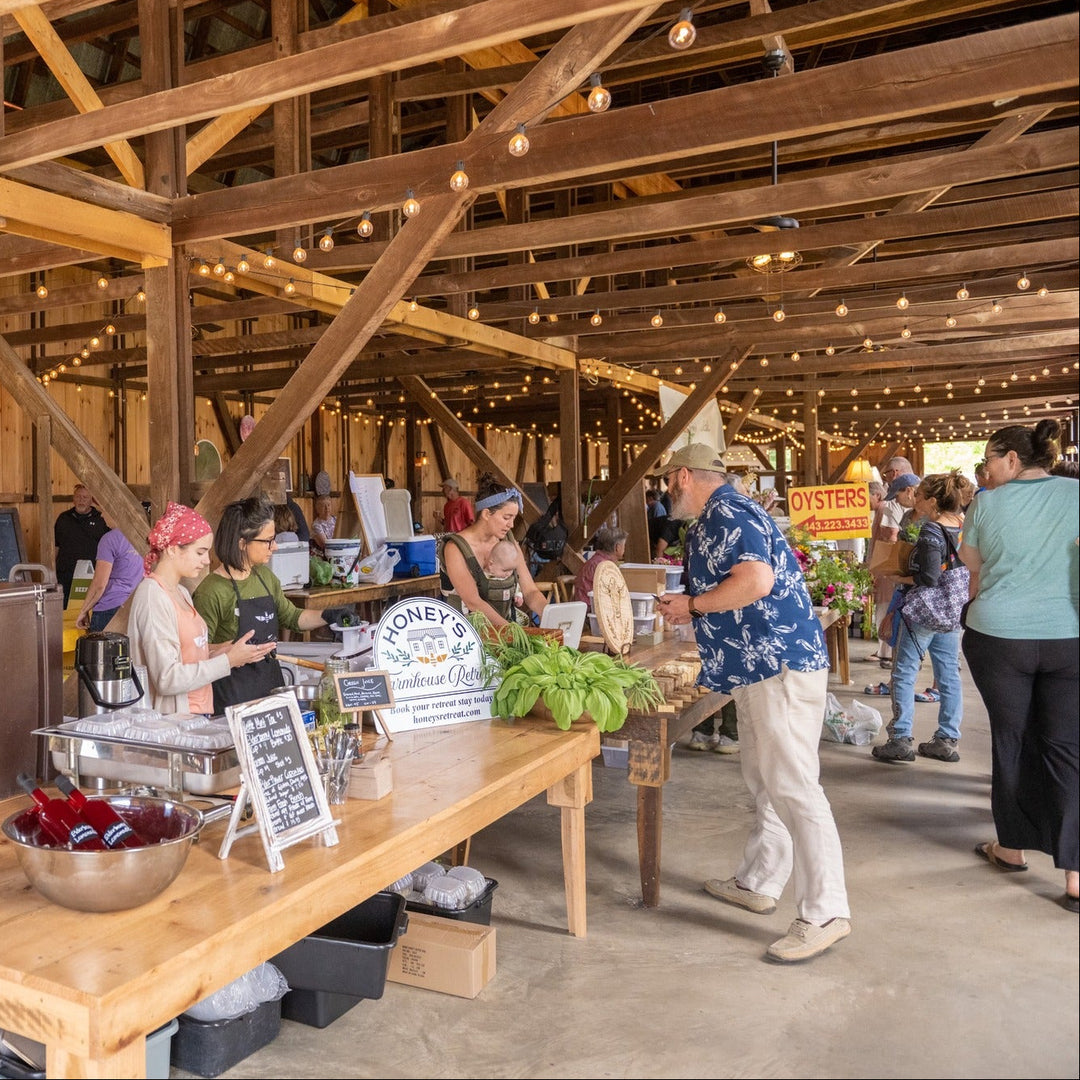 Vendors set up at wooden tables inside a barn with bistro lighting