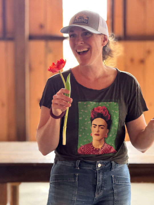 Person wearing a t-shirt with a Frida Kahlo graphic, holding a flower.