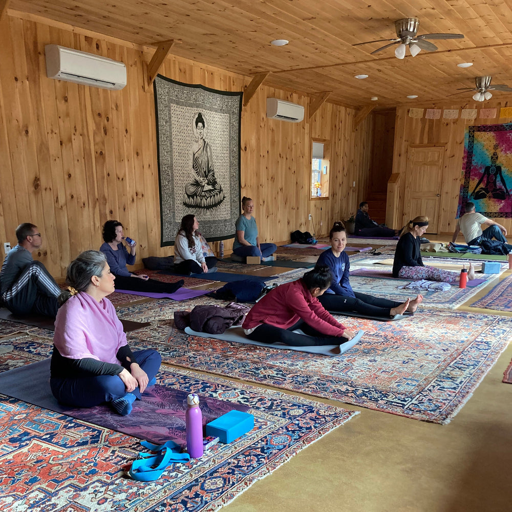 Group of people practicing yoga in a wooden room with tapestries on the walls.