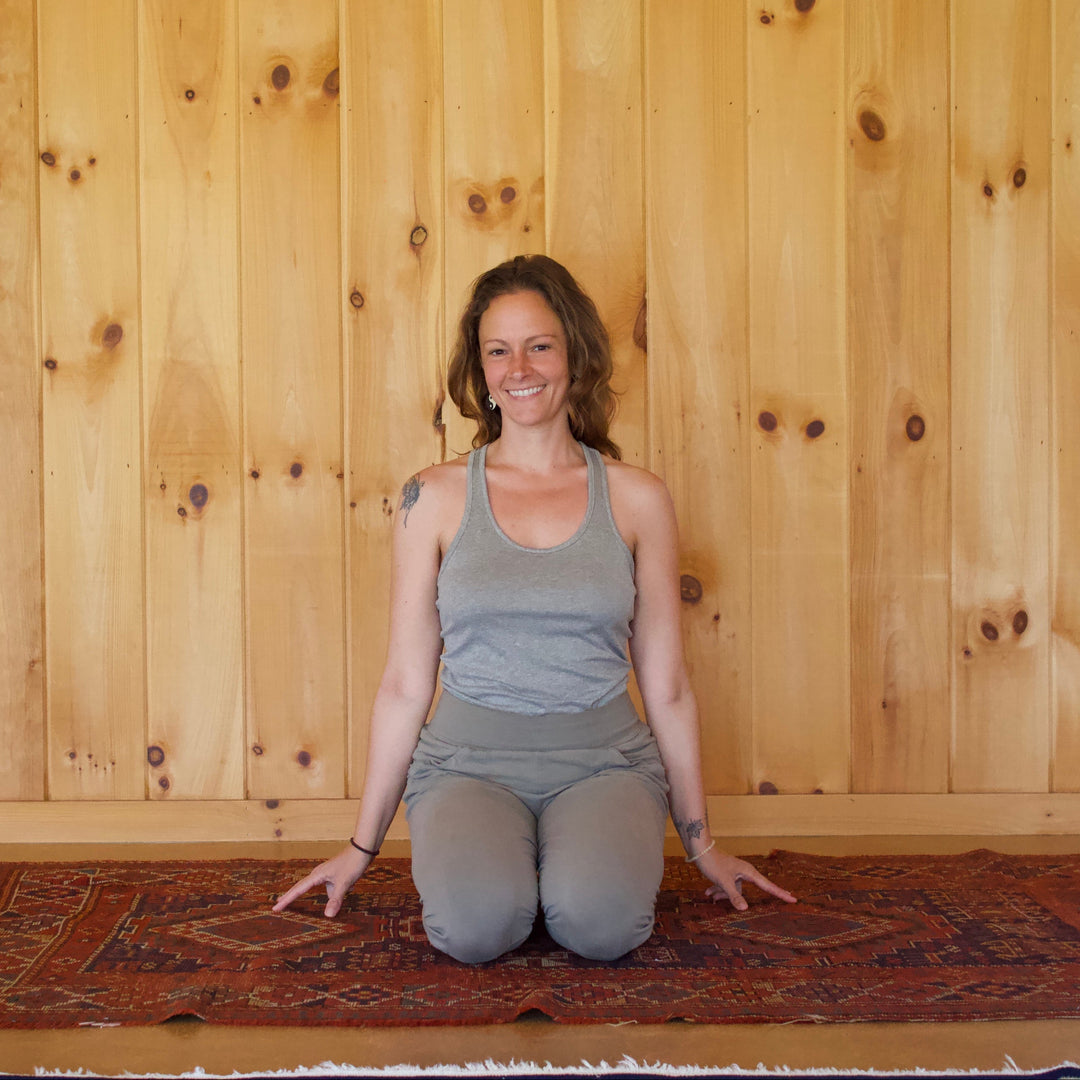 Woman sitting on a rug in front of a wooden wall