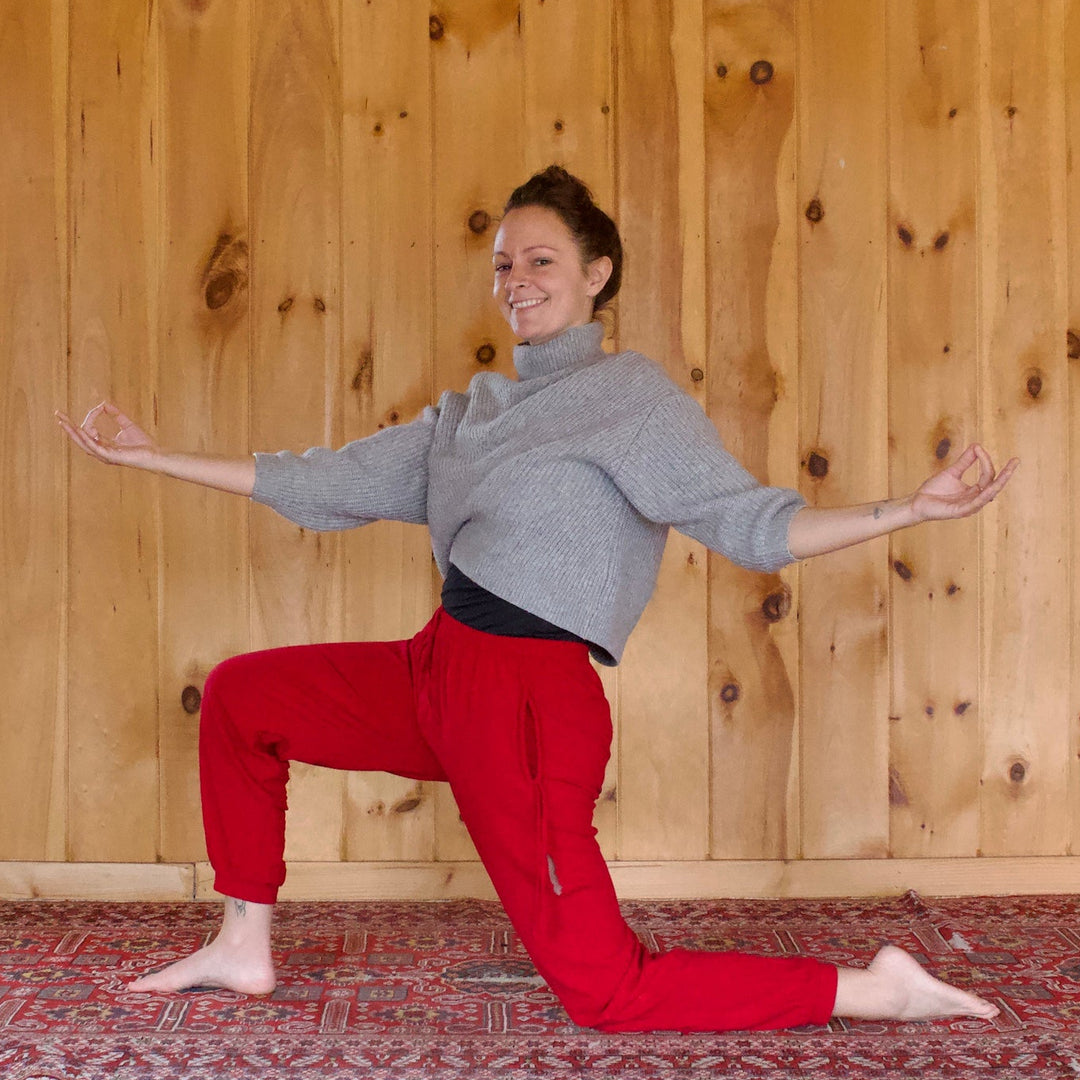Woman wearing red pants doing a lunge with a wooden wall in the background.