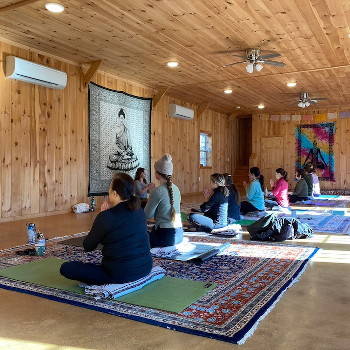 Group of people practicing yoga in a wooden room with colorful tapestries.