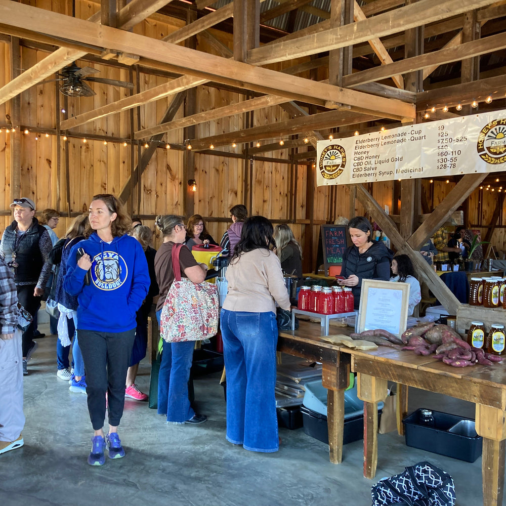 People inside a wooden barn with a table displaying jars and a banner.