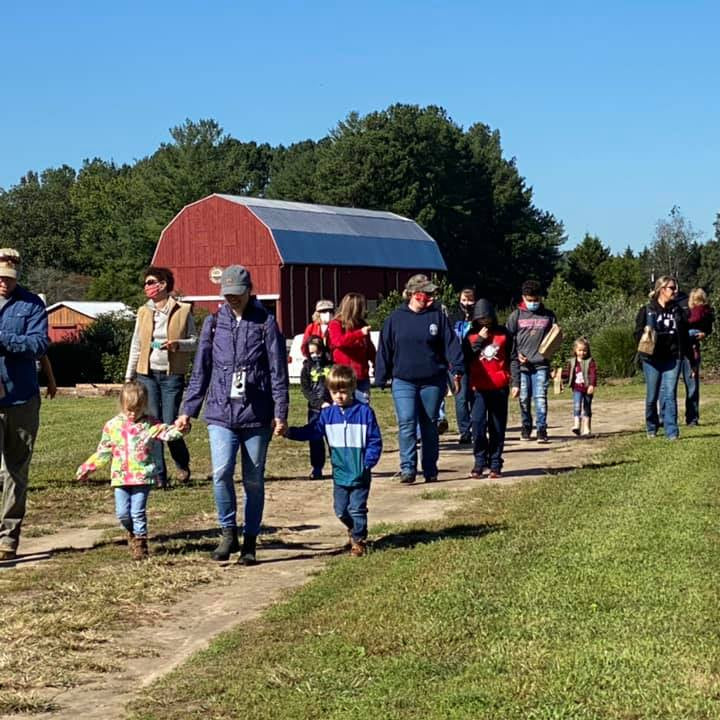 Group of people, including children, walking on a path near a red barn with a clear blue sky.