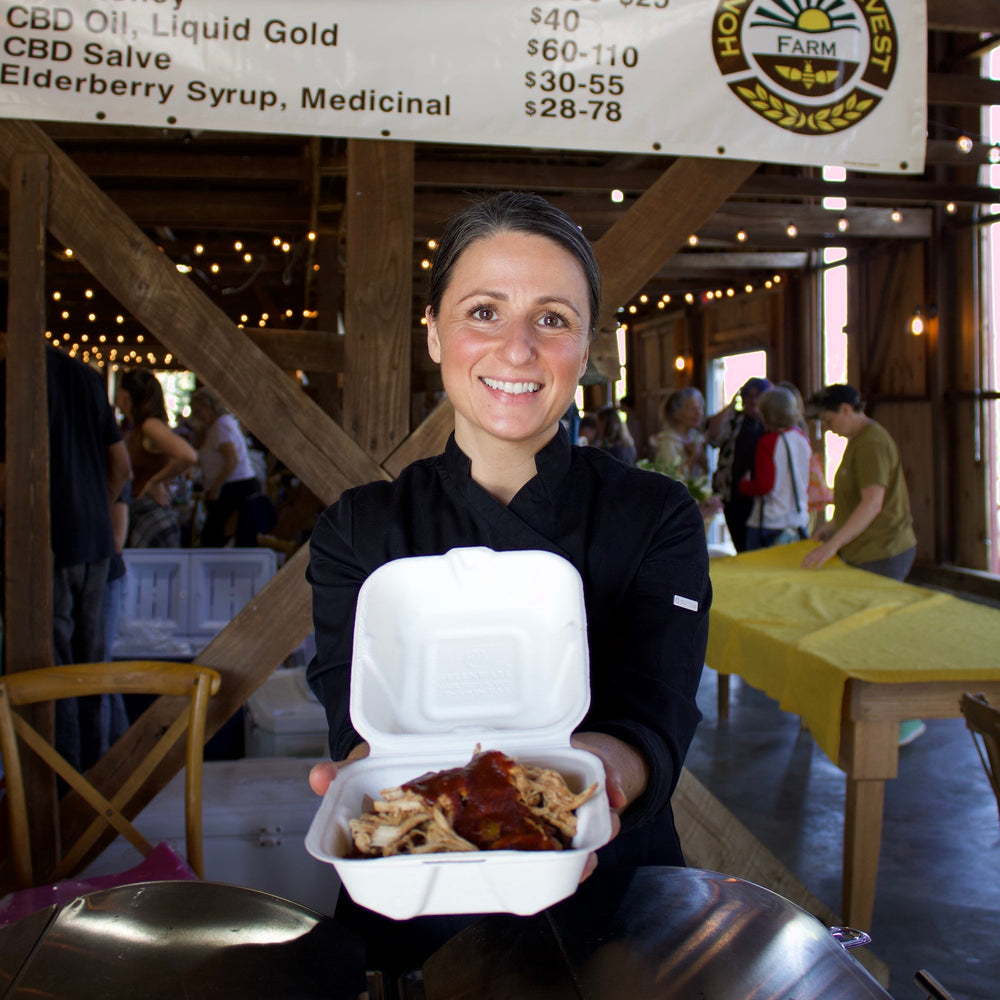 Person holding a take-out container with food in a casual setting, with a sign in the background.