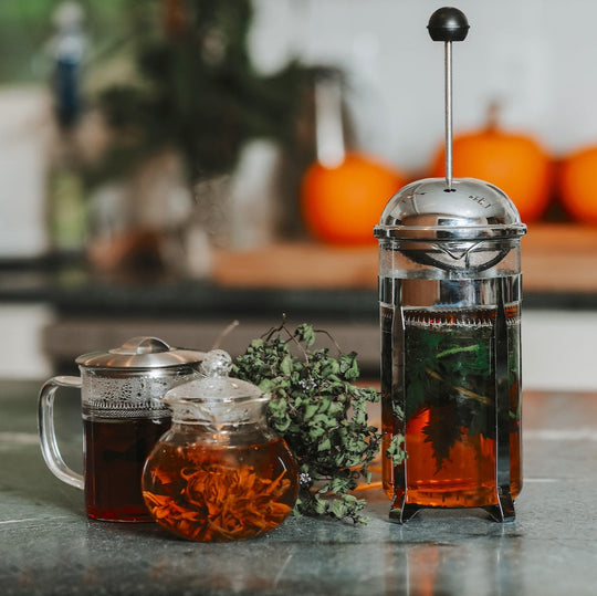Tea-making setup with a French press, teapot, and mug on a kitchen counter with pumpkins in the background.