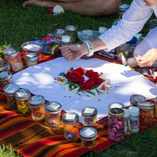 People sitting on grass with a spread of jars, flowers, and a blanket.
